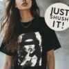 Provocative black and white tee featuring a grunge-style woman with a beanie and the phrase 'Just shush it', surrounded by small flowers.