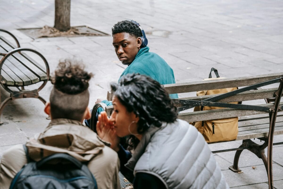 A group of young people sitting on a bench, sharing secrets and wearing streetwear, capturing urban vibes and community interaction.